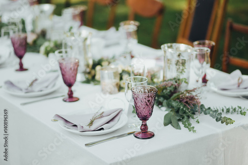 Festive table served dishes and decorated with branches of greenery, stands on green grass in the area of wedding party