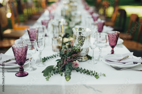 Festive table served dishes and decorated with branches of greenery, stands on green grass in the area of wedding party