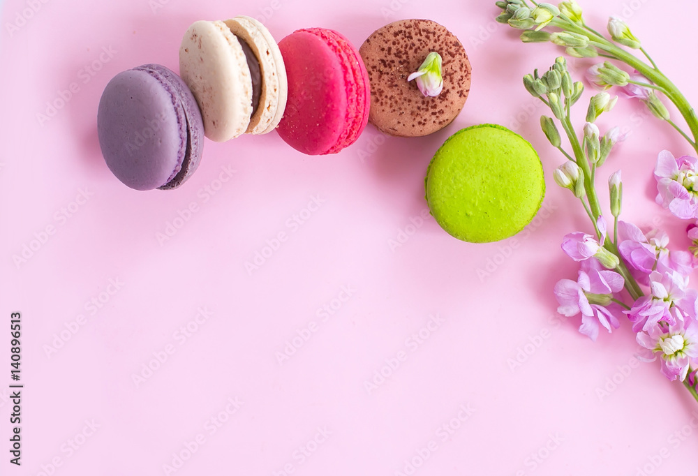 Obraz premium Multicolored macaroons сakes and flowers on a pink background.