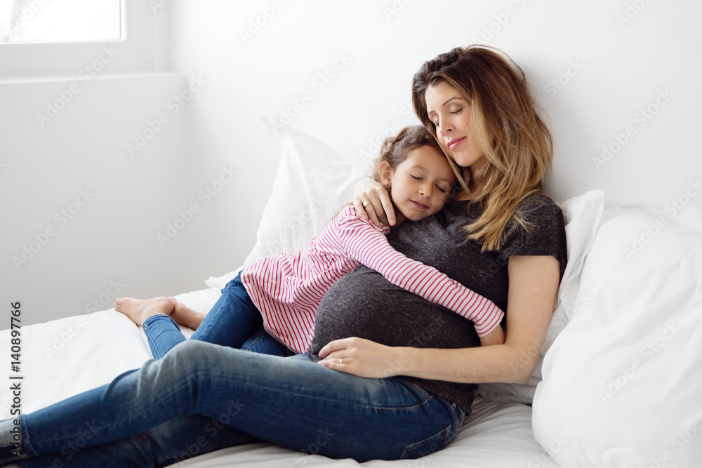 pregnant mother and her daughter cuddling on the bed with their eyes closed pregnant mother and her daughter cuddling on the bed with their eyes closed