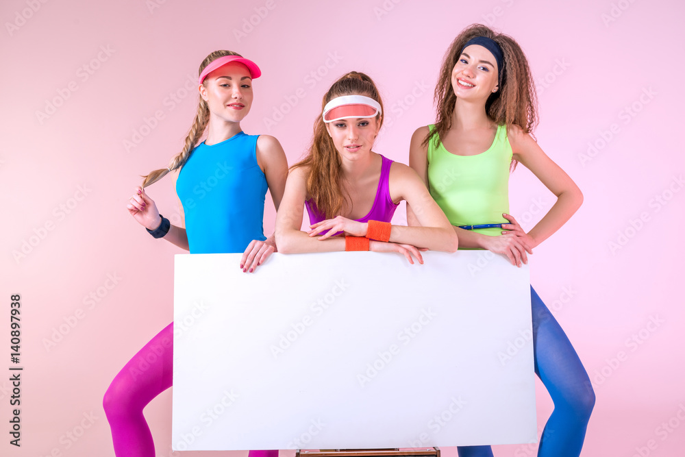 sporty women in fitness clothing holding banner on pink sporty women in fitness clothing holding banner on pink