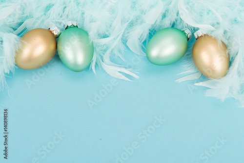 Decoration glass yellow and green easter eggs and blue feathers on a blue background with space for text