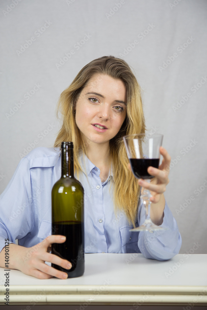 Young Caucasian white woman sitting at a table while drinking wine. She is blonde and pretty with light brown eyes. The background of the image is white. Young Caucasian white woman sitting at a table while drinking wine. She is blonde and pretty with light brown eyes. The background of the image is white.