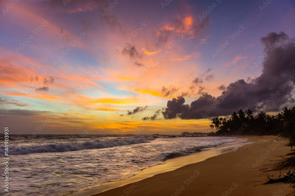 Colorful cloudy sky over the Indian ocean shore at sunset. Wijaya beach, Sri Lanka.