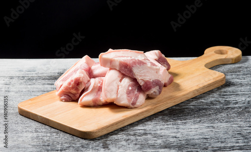 Pork belly on a wooden board over black background.