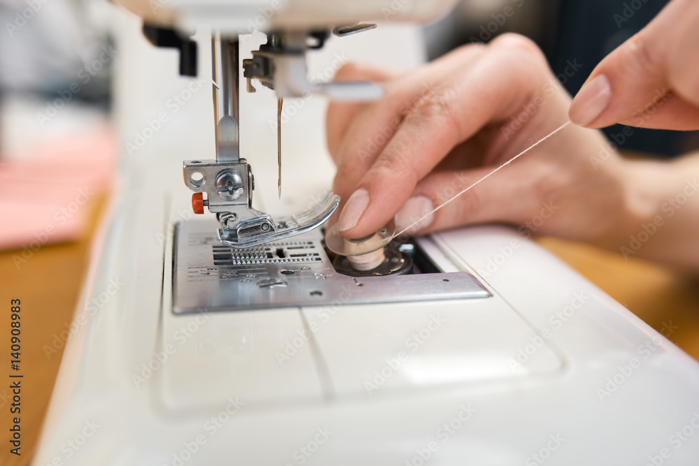 Female tailor threading bobbin into sewing machine case