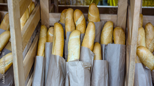 Fresh baked rustic bread loaves in paper bags on wooden shop shelf photo