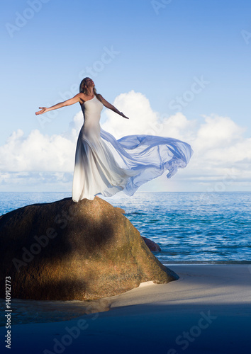 Beautiful slim woman in flying white dress at sandy beach