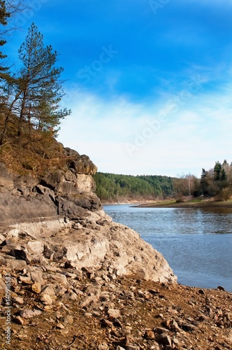 Steep and rocky river bank with river and wood.
