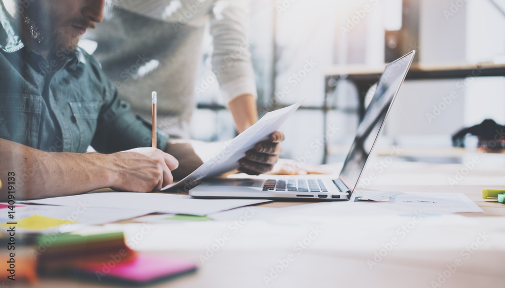Account manager working process.Young coworkers work with new startup project in office.Analyze document, plans.Modern laptop on wood table, papers, documents.Horizontal, blurred, flare.