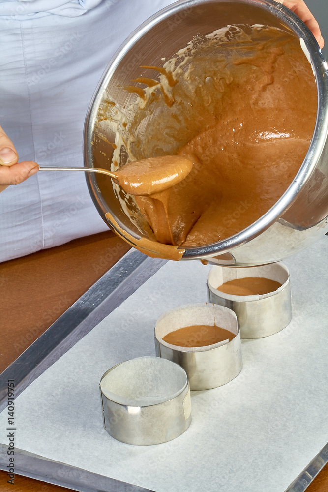 The cook pours the dough into forms for making cupcakes The cook pours the dough into forms for making cupcakes