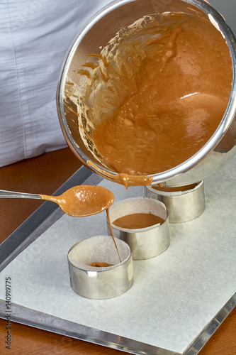 The cook pours the dough into forms for making cupcakes