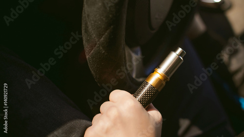 young vaper man with beard vaping mechanical mod. Guy smokes an electronic cigarette by blowing a smoke vapor. Holds in hand Sitting at the wheel of a car background