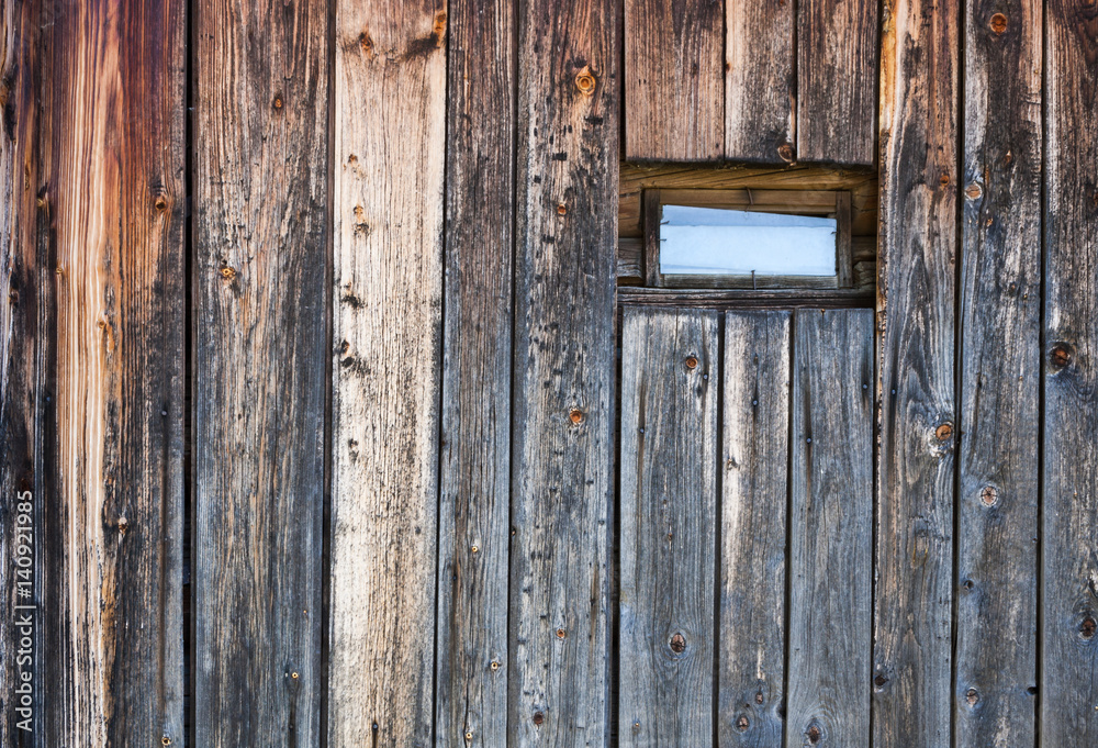 Wall of old weathered wooden planks with small window on it.