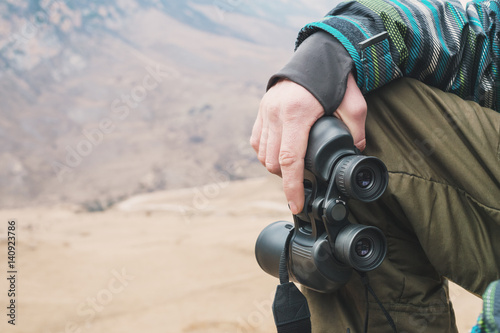 Large binoculars in the man's hand of a traveler who is in the mountains © yanik88