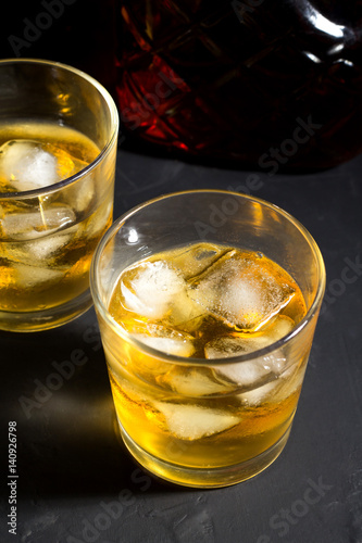 Whiskey with ice in glasses on a black background.