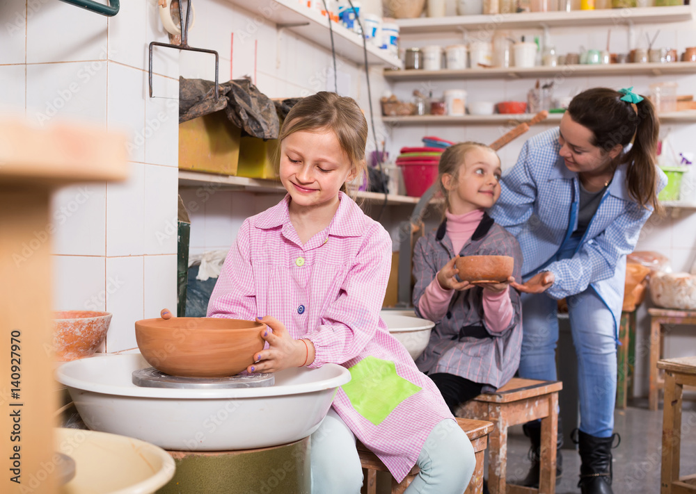 teacher helping teenagers at making pottery during arts and crafts class