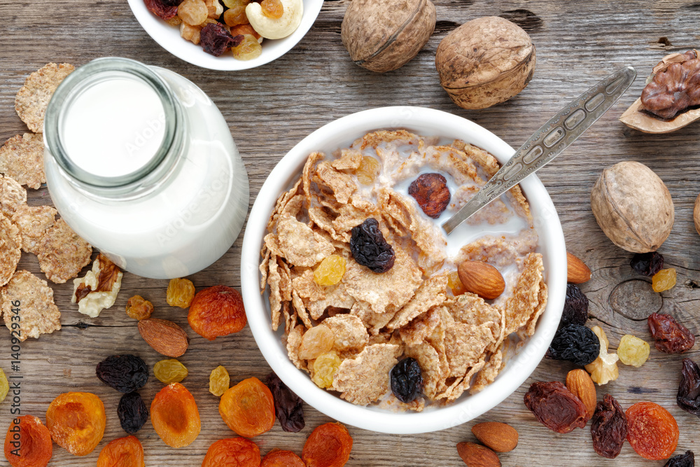 Healthy breakfast: cereal wheat flakes with milk in bowl, dried fruits, muesli and milk bottle on wooden table. Top view, flat lay. Healthy breakfast: cereal wheat flakes with milk in bowl, dried fruits, muesli and milk bottle on wooden table. Top view, flat lay.