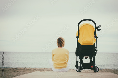 Картината върху платно Mother sitting alone next baby stroller on beach by the sea