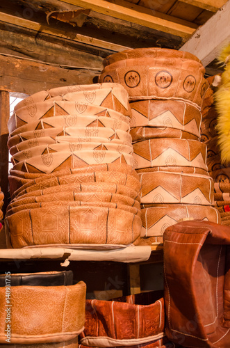 Handmade leather poufs stacked high in small traditional craft shop in soukh of Fez, Morocco