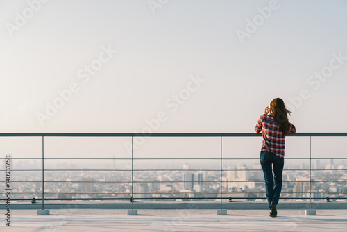 Woman using mobile phone at rooftop during sunset with copy space, communication or lonely people concept photo