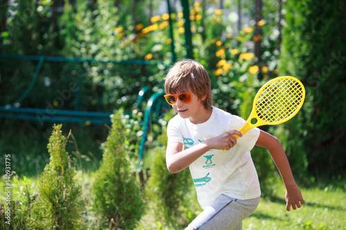 Cute boy wearing orange sunglasses plays beach tennis in the garden
