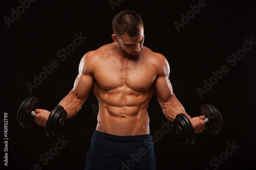 Muscular handsome man is training with dumbbells in gym. isolated on black background with copyspace © satyrenko