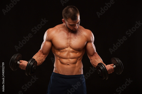 Muscular handsome man is training with dumbbells in gym. isolated on black background with copyspace