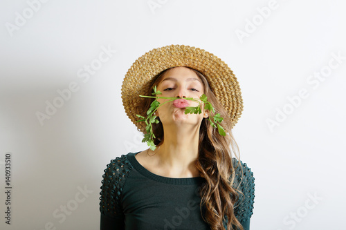 Girl in straw hat with parsley on the face, fun and healthy lifestyle