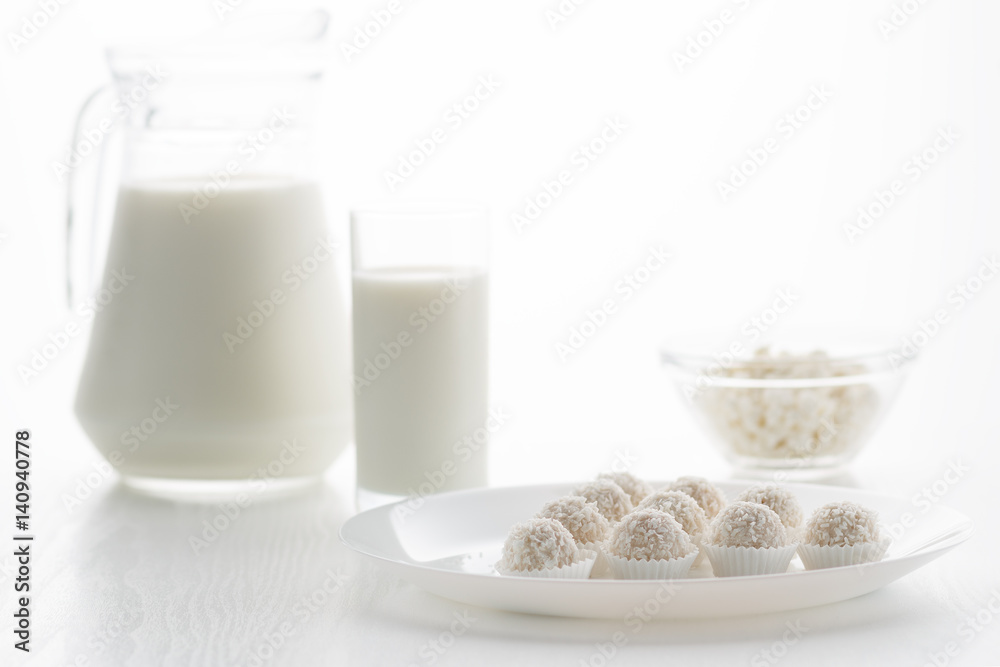 Raffaello candy in baskets on a plate, with milk in a glass and jug, cottage cheese in a bowl in the background, on a white table, in a high key, with space for text Raffaello candy in baskets on a plate, with milk in a glass and jug, cottage cheese in a bowl in the background, on a white table, in a high key, with space for text