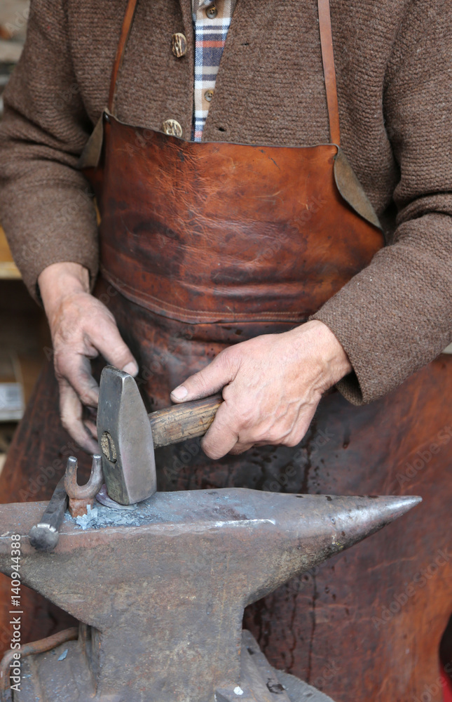hands of an elderly blacksmith working iron with a hammer and th