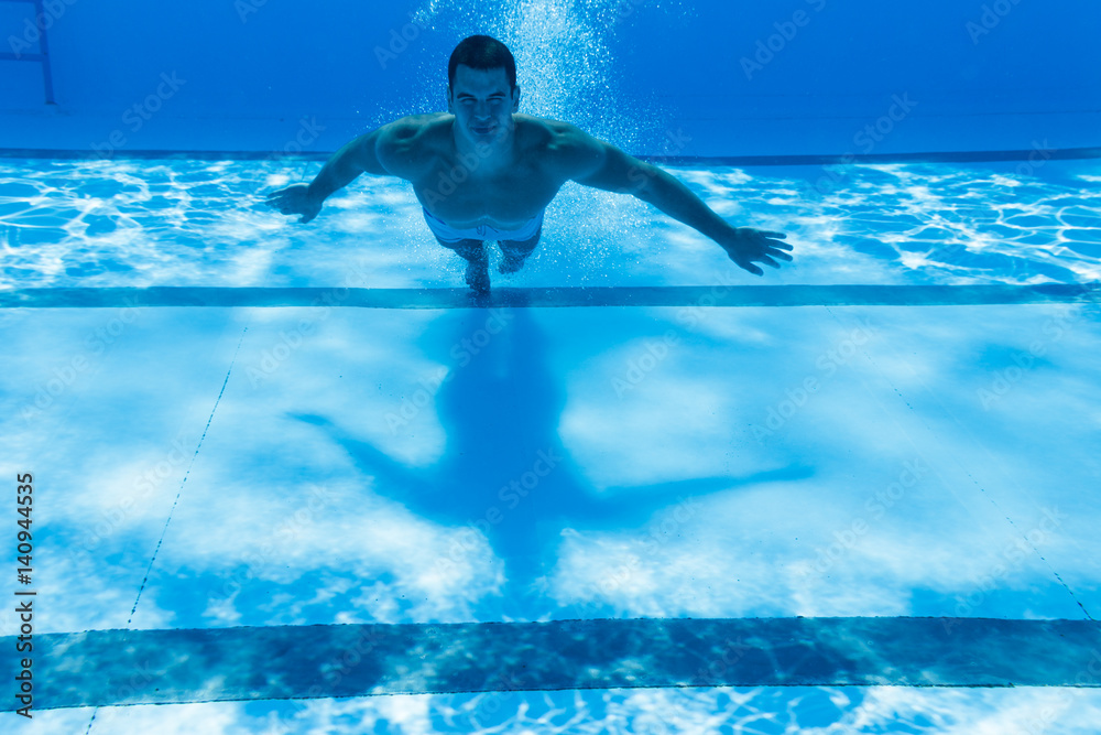 Underwater fun. Young handsome man swimming underwater and diving in the swimming poll. Sport and leisure.