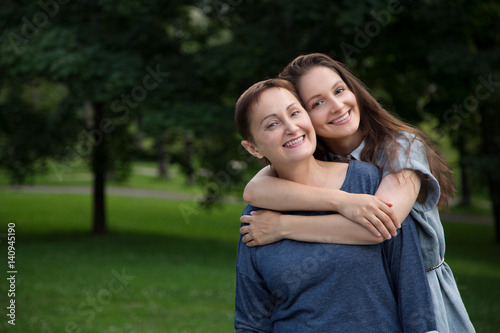 Mother and adult daughter hugging and having fun together in the park outdoor in summer. Portrait of happy women smiling and looking at the camera.