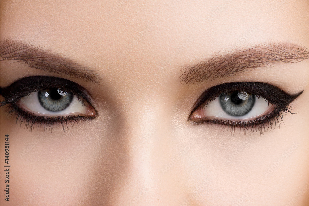 Fototapeta premium Beautiful woman with bright make up eye with sexy black liner makeup. Fashion big arrow shape on woman's eyelid. Chic evening make-up