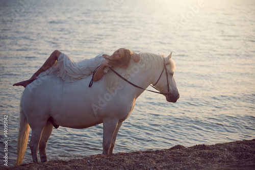 Girl in white dress with horse on the beach