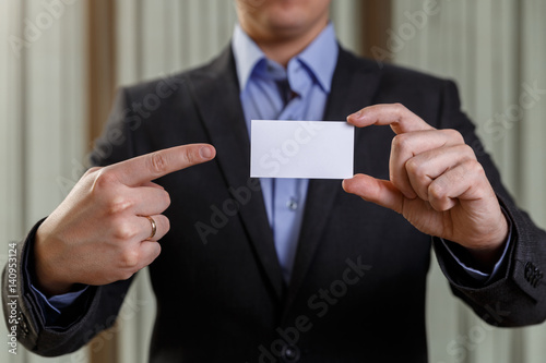 Businessman holding visit card. Man showing blank business card. Person in black suit points a finger. Mock up design.
