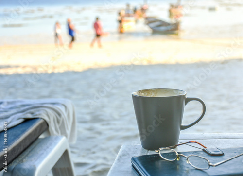 Hot cappucino coffee at the beach with background of people in activities,partly sipped..