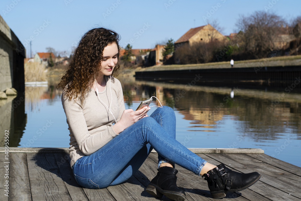 The girl listens to music next to the river