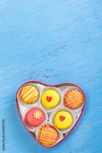Macaroon cakes. Colorful almond macaron cookies. Love heart-shaped delivery box. Different flavors. On blue wooden rustic background.