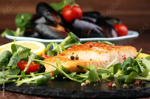 baked salmon grilled pepper lemon on a plate with lettuce leaves and tomato on wood background - healthy eating concept