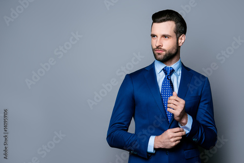 Fototapet Portrait of serious fashionable handsome man in blue suit and tie  buttoning cuf