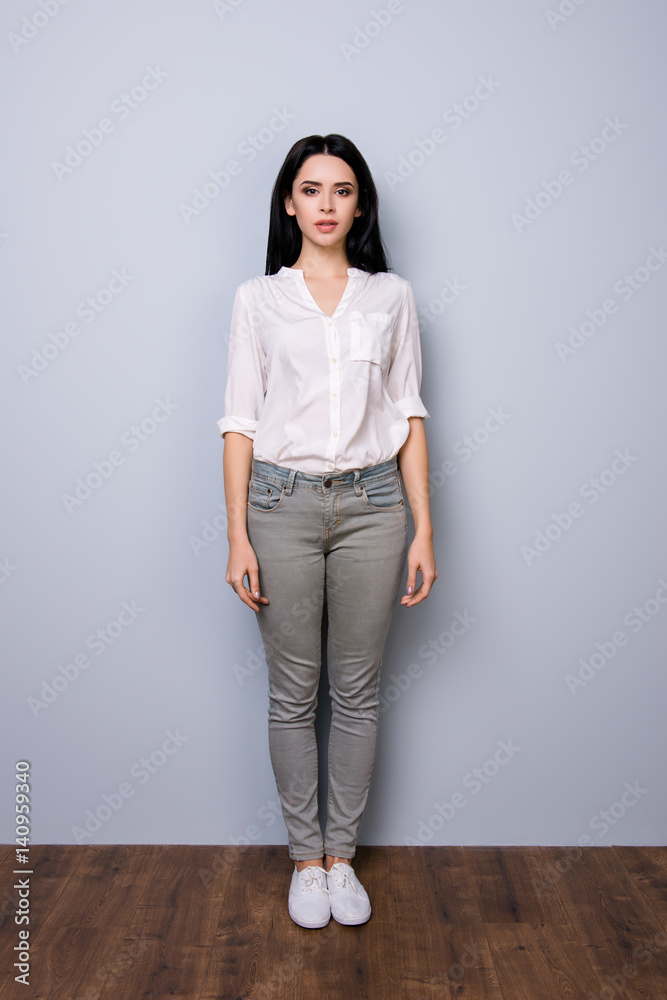Front view, full portrait of young charming calm lady with rolled up sleeves standing against gray background Front view, full portrait of young charming calm lady with rolled up sleeves standing against gray background