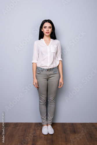 Front view,  full portrait of young charming calm lady with rolled up sleeves standing against gray background photo