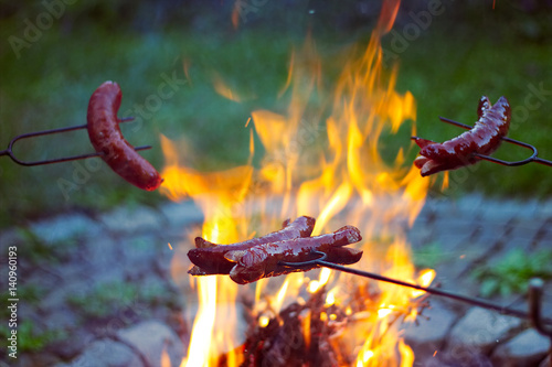 Grilling sausages over a campfire, campers roasting sausages on toasting forks 
