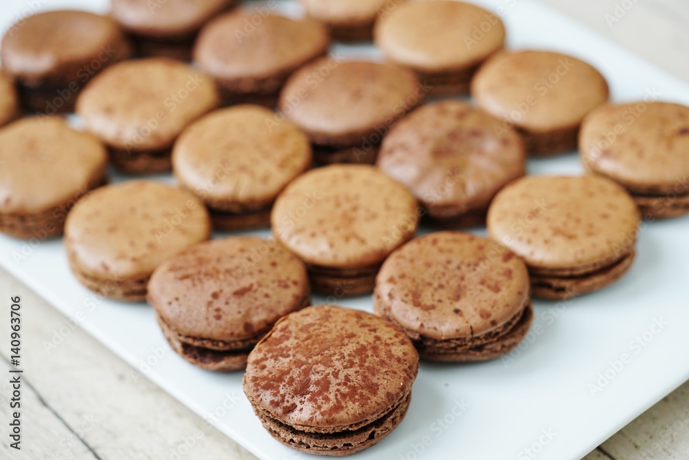 Chocolate round macaron cookies on a white platter Chocolate round macaron cookies on a white platter