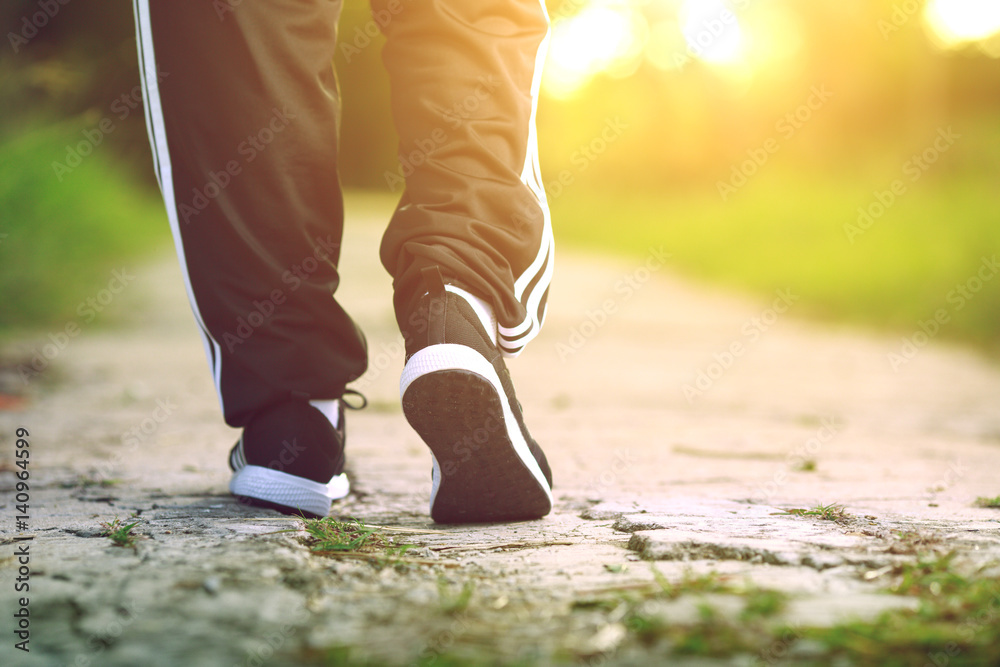 Runner feet running on concrete road in park - fitness sunrise jog workout welness concept