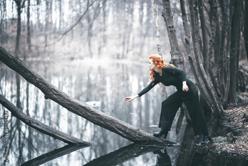 beautiful girl with red hair standing next to the forest lake