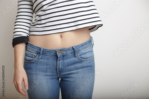 Young girl in blue jeans and a striped sweater and raised her hand bare belly with a beautiful waist and umbilicus © koldunova
