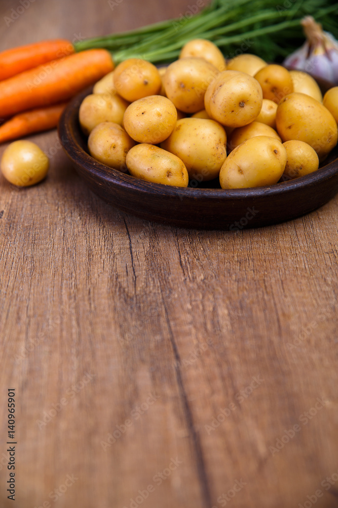 Potatoes in plate. Carrot, garlic and raw new potato. Fresh natural vegetables. Organic bio food on rustic wooden table. Potatoes in plate. Carrot, garlic and raw new potato. Fresh natural vegetables. Organic bio food on rustic wooden table.