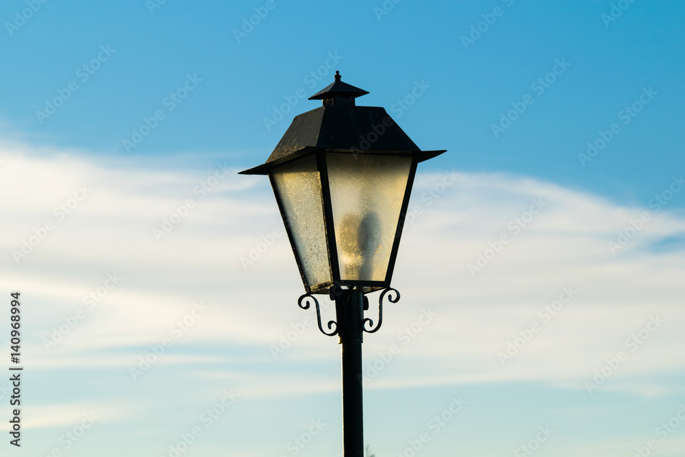 Head of an old fashioned style lamppost against a blue sky Head of an old fashioned style lamppost against a blue sky